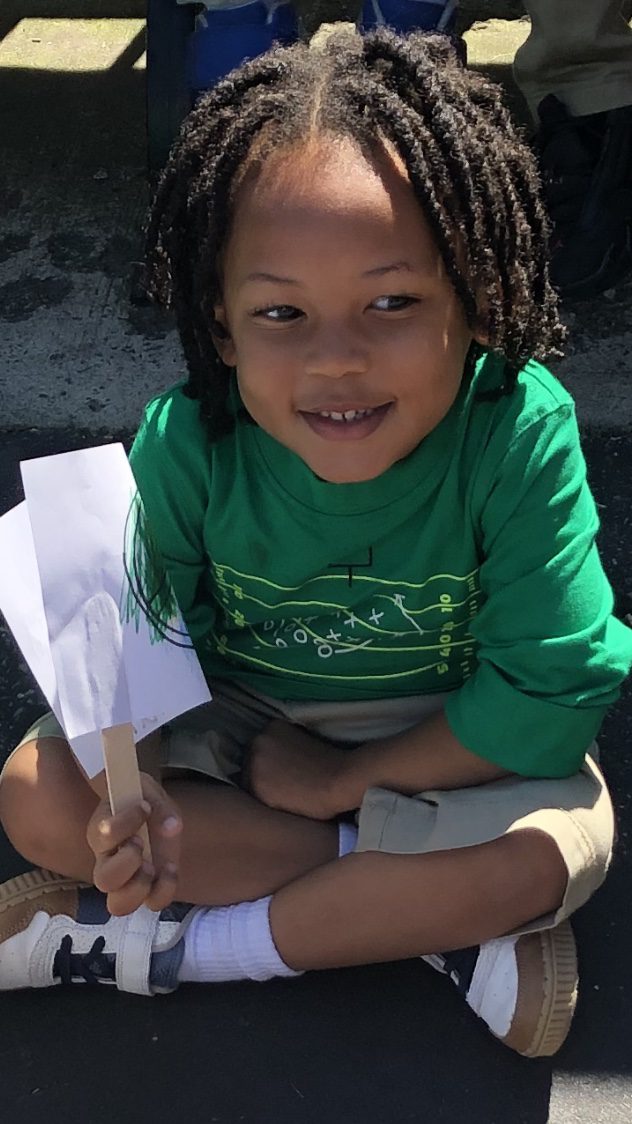 Child sitting on the ground with an art project in their hand.